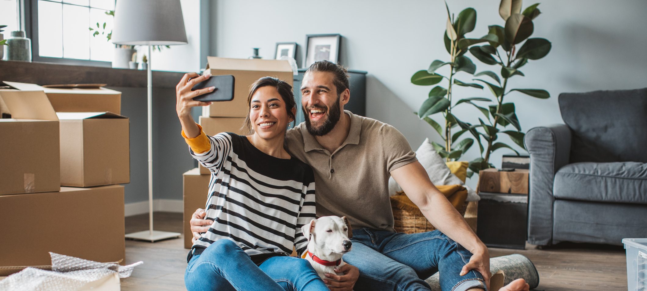 Young couple moving in new house. They are happy and making selfie with their pet dog.